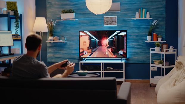 Caucasian gamer playing action games on tv console using wireless joystick with modern technology. Young man of simulator enjoyment gaming on electronic devices as hobby and leisure