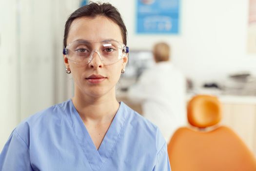Close up of woman nurse in uniform looking into camera while working in stomatology hospital office. Medical team waiting sick patient to start dental surgery during stomatological appointment