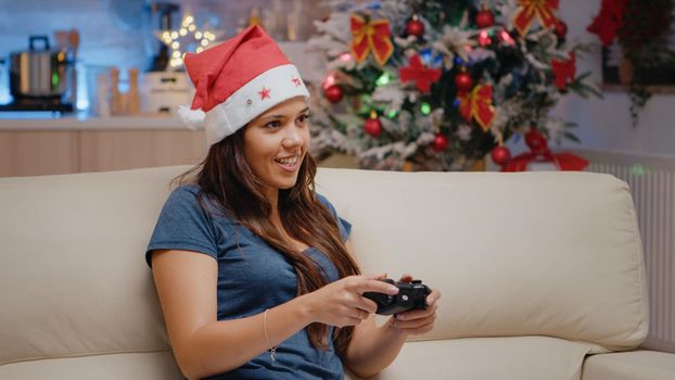 Close up of woman winning video games on TV console with joystick on christmas eve holiday. Festive person with santa hat feeling happy and playing online with controller on television.