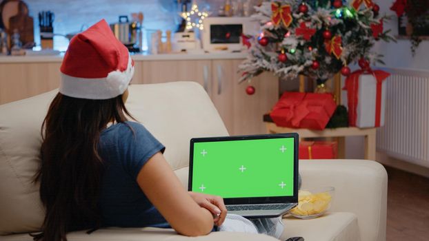 Woman looking at horizontal green screen on laptop on christmas eve. Festive adult watching chroma key on device, having mockup template and isolated background. Person with gadget