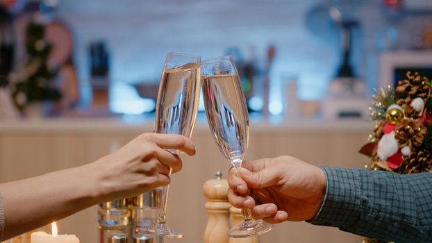Close up of couple clinking glasses of champagne. People sitting at table for festive dinner on christmas eve, celebrating holiday with chicken and alcohol. Festivity with seasonal meal