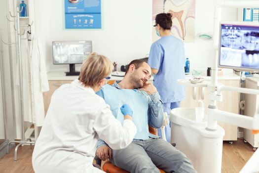 Stomatologist senior woman examining patient tooth pain during stomatology consultation. Sick man sitting on dental chair preparing for dentistry surgery waiting for toothache treatment