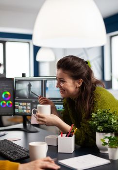 Happy videographer editing video project drinking coffee using post production software working in digital multimedia company with dual monitors setup. Retoucher processing audio film montage on pc