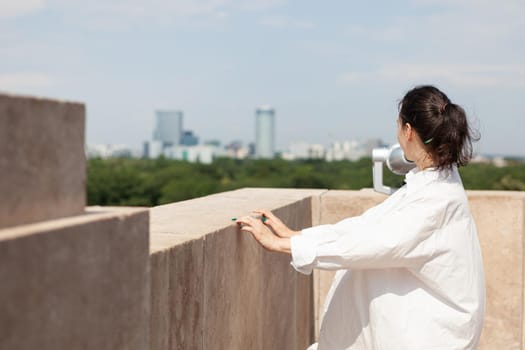 Woman standing on tower rooftop enjoying summer vacation looking at panoramic view of metropolitan city. Landscape with urban buildings seeing from bulding observation point. Travel concept
