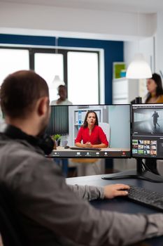 Video editor talking with remote customer in web online meeting using video call editing project, getting feedback on commercial movie using post production program on two displays in creative agency