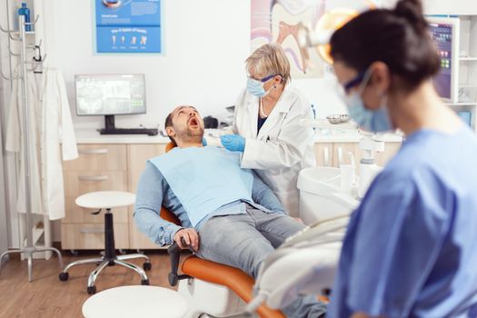 Stomatologist senior doctor looking in patient mouth preparing for stomatology inspection. Stomatological nurse preparing stomatology tools working in stomatological clinic office