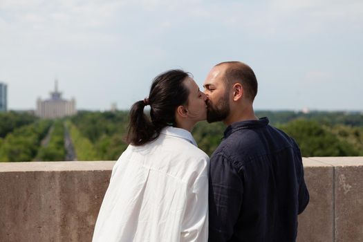 Romantic couple celebrating relationship anniversary kissing on tower terrace enjoying spending time together during vacation. View of city skyline from observation point. Panoramic view of buildings