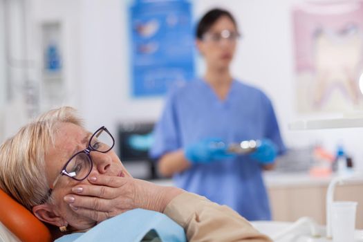 Elderly patient in pain at dentist clinic waiting diagnosis from doctor in medical office. Senior woman in healthcare hospital accusing and complaining about tooth.