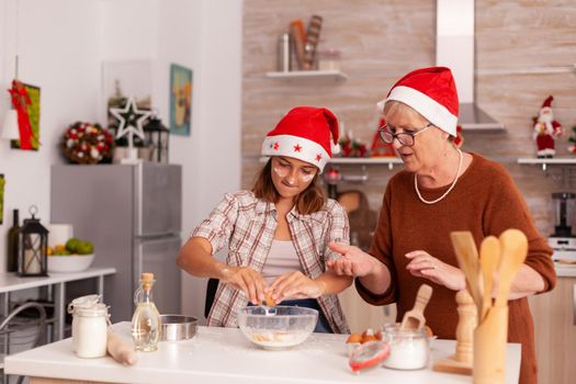 Child breaking eggs in bowl making homemade traditional cookies dough cooking xmas delicious gingerbread dessert with senior woman. Happy family celebrating christmas season enjoying winter season