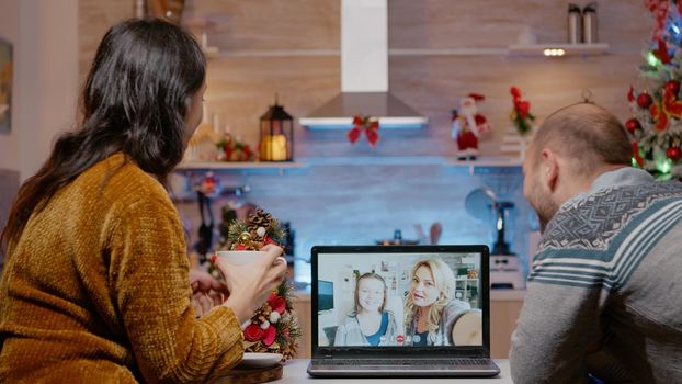 Couple using video call communication with family for christmas eve celebration. Festive people talking to adult and child feeling cheerful for winter holiday. Online remote festivity