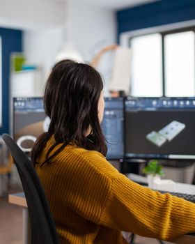 Young woman industrial engineer working at pc with two monitors, screens showing CAD software with 3D prototype of gears metalic mechanical piece. Employee working in creative agency office