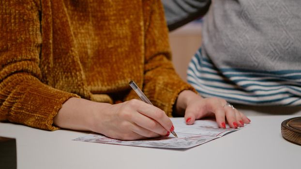 Close up of woman holding pen and signing christmas card for winter celebration. Couple writing festive postcard on christmas eve preparing for holiday festivity with relatives and friends.