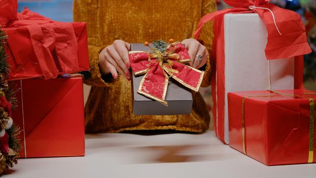 Close up of hand holding present box with ribbon and bow tie for christmas eve festivity. Woman with gifts for family preparing for holiday celebration in december. Seasonal gift