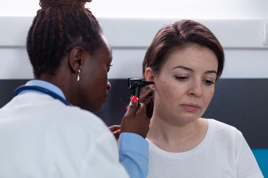 African american otologist doctor holding medical otoscope analyzing sick woman patient ear working in hospital office during clinical appointment Therapist discovering otology infectitb