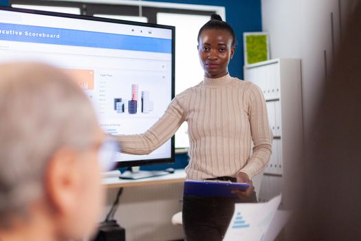 African leader briefing business organization pointing at graph briefing teamwork. Corporate staff discussing new business application with colleagues looking at screen