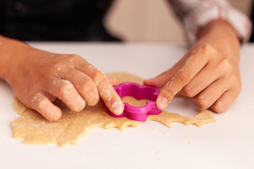 Closeup of grandchild hands making homemade cookie using xmas dough shape celebrating christmas holiday in x-mas decorated kitchen. Child enjoying winter season cooking gingerbread dessert