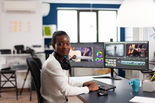 Black videographer smiling at camera editing video project in post production software working in creative studio office. African movie maker editing audio film montage on professional computer