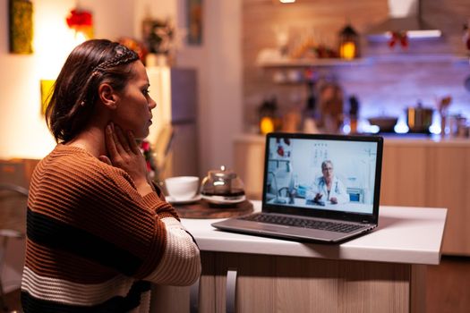 Woman with sickness calling doctor on online video conference while sitting in festive kitchen at home. Ill young patient using telemedicine for healing treatment and healthcare advice