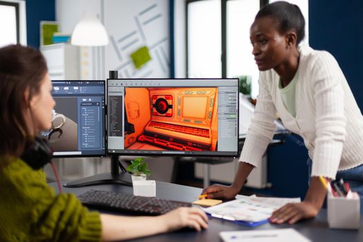 Multiethnic women game designer looking at computer with dual displays working together at project in studio office. Gamer workers developing new online video games on pc with modern technology