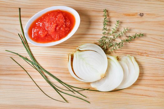 Fresh tomato sauce in bowl with slices of white onion , twigs of thyme and chives on wooden background , preparing food 