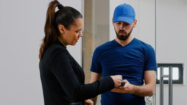 Delivery guy bringing takeaway food meal holding POS terminal service in startup business company office. Businesswoman receiving lunch order paying with contactless credit card during lunchtime