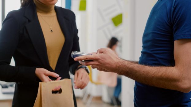 Closeup of businesswoman paying food order having contactless payment with smart watch using POS terminal service. Delivery guy worker bringing takeaway food lunch order during lunchtime at workplace