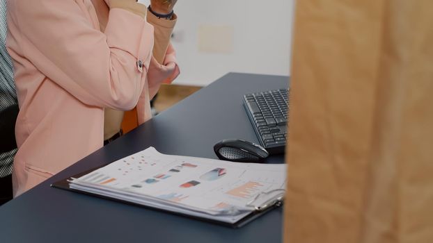 Executive manager having takeaway meal order eating tasty sandwich during lunchtime in startup business office. Businesswoman drinking coffee analyzing statistics having lunch break