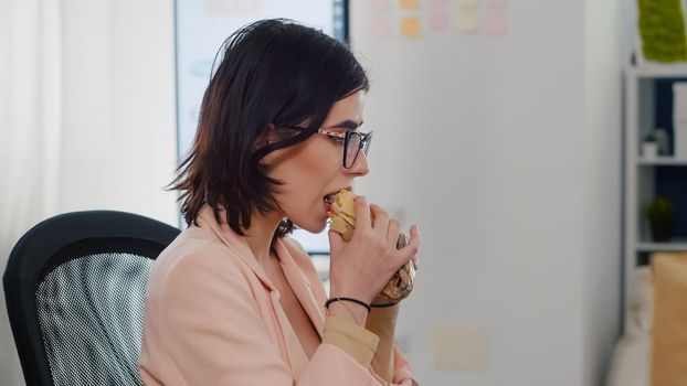 Entrepreneur woman eating tasty sandwich having work break working in business company office during takeout lunchbreak. Fast food order paper bag delivered. Woman typing strategy on computer