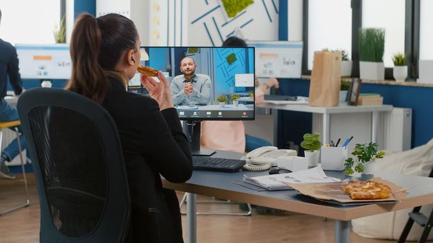 Executive manager eating pizza slice discussing with remote collegue during online videocall meeting conference. Takeout order food delivery in corporate place, meal break package delivered at office.