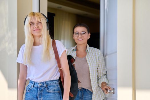 Mom and daughter student on porch of house near front door. Mother and female teenager in headphones with backpack going to college. Education lifestyle relationship parent teen child adolescence, Bye