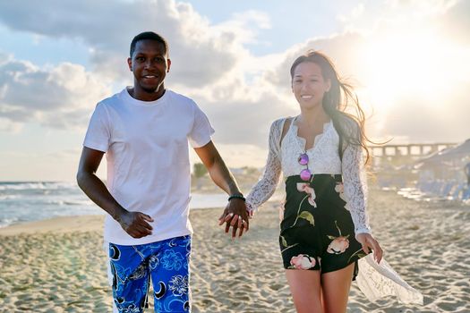 Beautiful young multiracial couple running along beach together. Happy loving african man and asian woman holding hands. People, love, happiness, relationship, multiethnic family, vacation, tourism