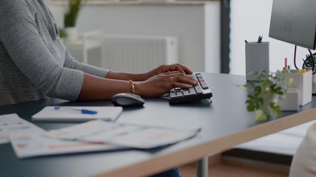 Close-up of teenager with dark skin hands on keyboard typing email on computer working at education article sitting at desk table. Student woman browsing information news in living room