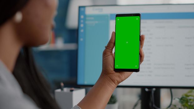 Close-up of african woman holding mock up green screen chroma key phone with isolated display in hands having online videocall conference meeting. Student working remote from home watching video