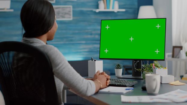 African american woman working remote from home listening school professor explaining online course. Student looking at mock up green screen chroma key display during virtual videocall meeting conference