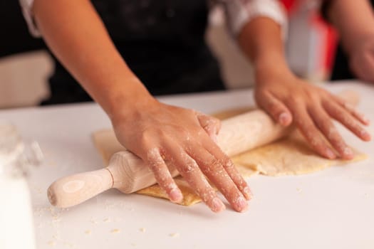 Closeup of granddaughter hands preparing homemade gingerbread using rolling pin making cookies dough celebrating christmas holiday. Child cooking delicious xmas dessert enjoying winter season