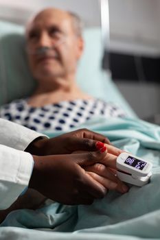 Caring friendly african american doctor therapist holding sick senior patient hand, comforting, showing comapssion, talking about treatment, while he's breathing with help from oxygen mask.