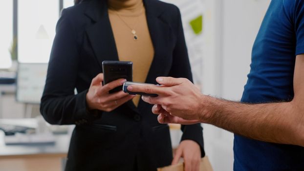 Closeup of delivery man holding takeaway food order meal bringing at company office workplace during takeout lunchtime. Businesswoman paying lunch with smartphone using POS contactless