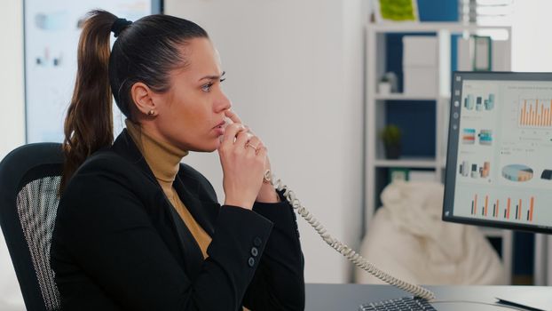 Multitasking executive manager talking at landline explaining company graphs to remote collegue while having takeaway delivery food order. Manager eating tasting pizza slice during takeout lunchtime