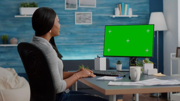 African american student sitting at desk working remote from home during virtual videocall meeting conference. Black woman browsing school information using mock up green screen chroma key computer