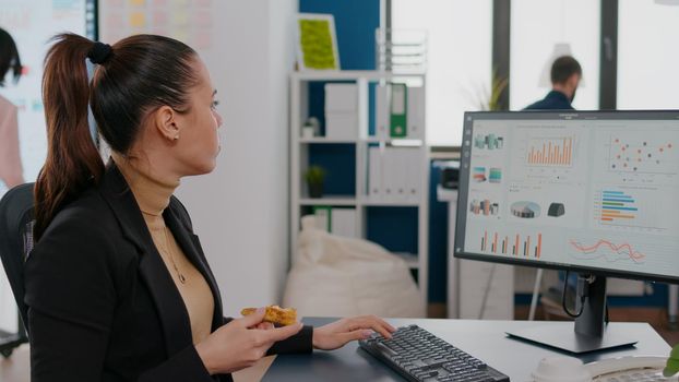 Businesswoman having delivery food order on desk during takeout lunchtime working in business company office. Entrepreneur woman eating takeaway lunch pizza slice typing management statistics