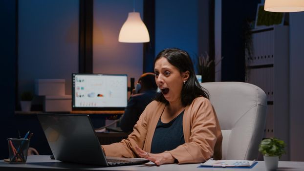 Joyful successful businesswoman enjoys receiving good news winning business job late at night. Happy entrepreneur working in startup company office smiling while reading promotion email