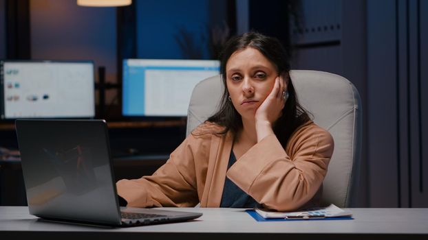 Portrait of exhausted workaholic manager checking economic statistics using laptop computer while sitting at desk table in business company office. Tired businesswoman typing financial strategy