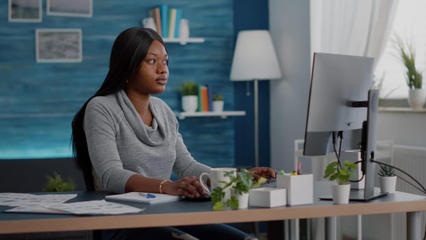 Student with black skin searching online courses writing school homework on on computer during online webinar education. Woman sitting at desk table in living room working remote from home