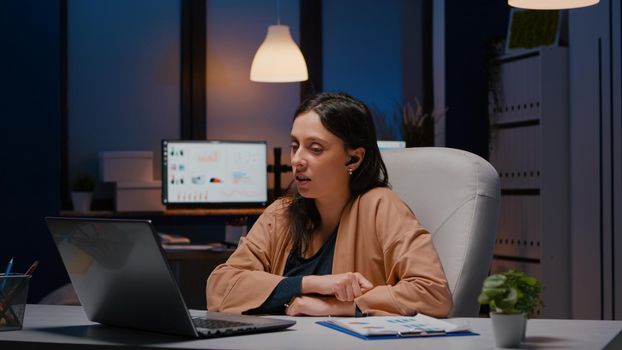 Businesswoman with headphones discussing marketing statistics planning business strategy. Entrepreneur woman talking with her collegues during online videocall conference company meeting in evening