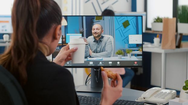 Executive manager eating delivery takeaway pizza during online videocall conference meeting discussing with remote coworker. Manager sitting at desk having takeout lunchtime in office