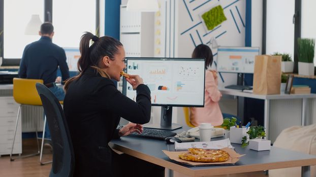 Executive manager eating tasty pizza while typing financial statistics at desk in workplace. Takeout order food delivery in corporate job place, lunch meal break package delivered at startup office.