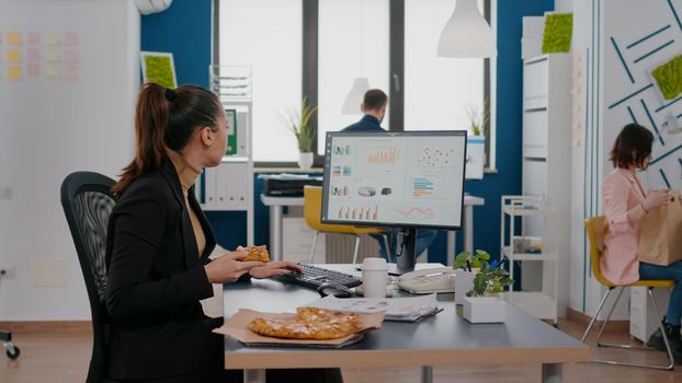 Businesswoman enjoying food meal order in company office during takeout lunchtime break working at financial graphs. Entrepreneur woman eating takeaway delivery pizza slice at desk