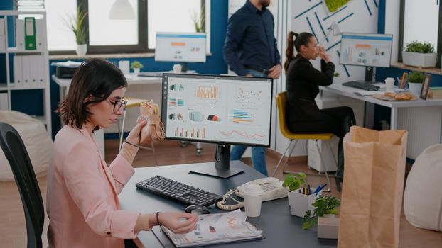 Entrepreneur woman having fastfood delivered meal order during takeout lunchtime working at company strategy in business office. Businesswoman eating delivery tasty sandwich at workplace