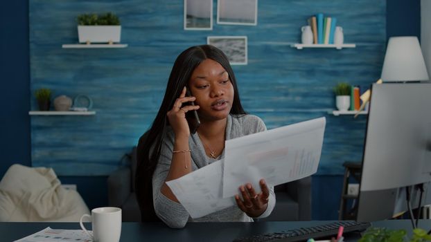 Upset student sitting at desk table in living room explaining high school homework discussing with collegue using smartphone. Black woman working at online webinar using academic elearning platform