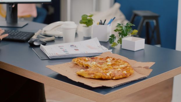 Closeup of executive manager taking slice of pizza eating in front of computer typing financial graphs in startup business company office. Businesswoman having takeaway fastfood order during lunchtime